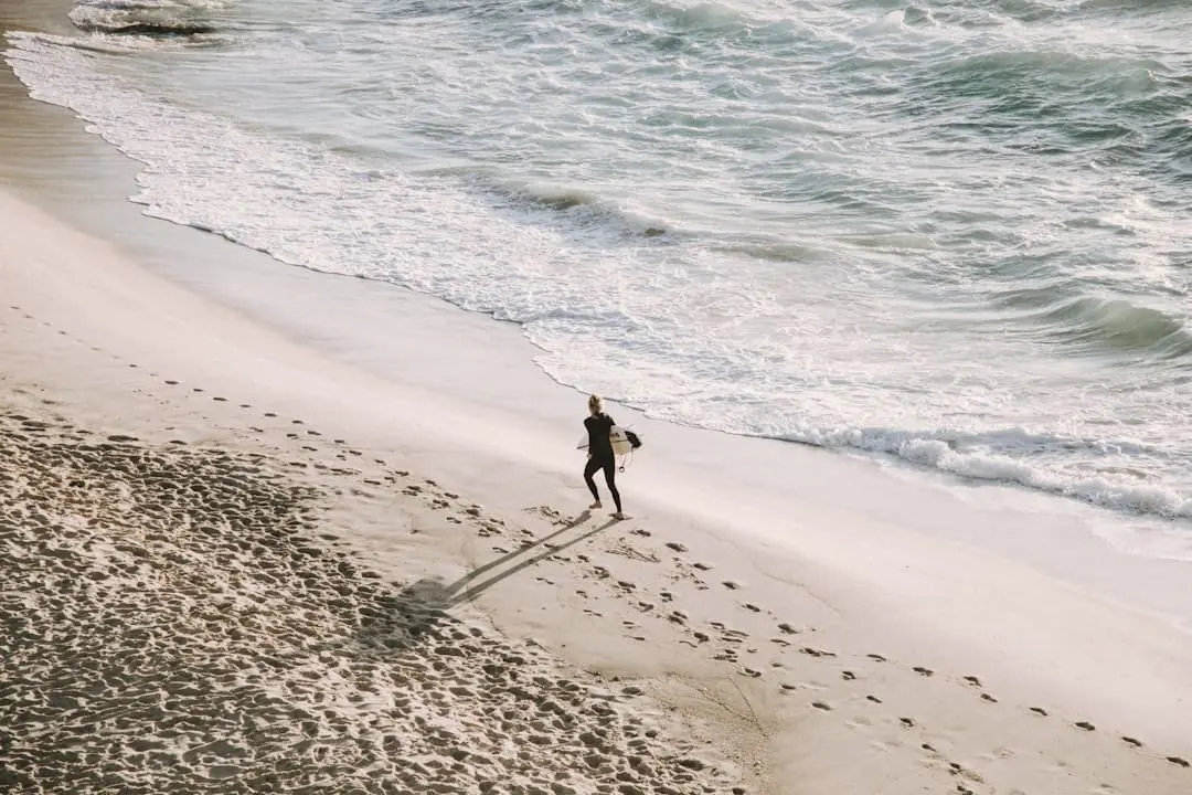 A surfer walks on a sandy beach.